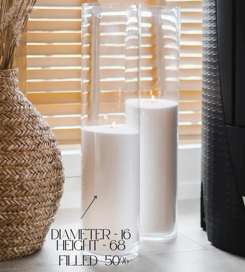 1. Two tall glass vases filled with white candle sand, lit wicks, placed near a woven basket and window blinds