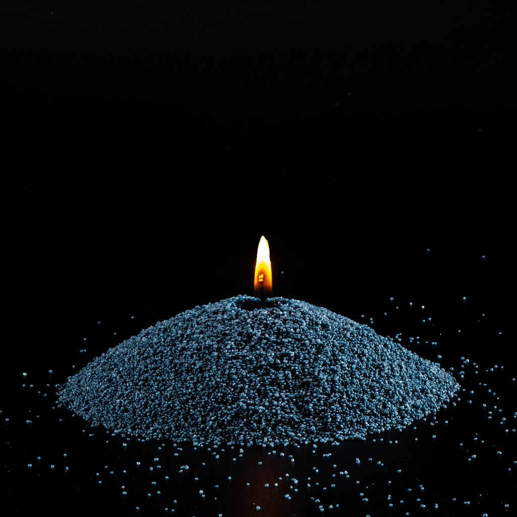 2. Mound of space grey candle sand with lit wick on black background