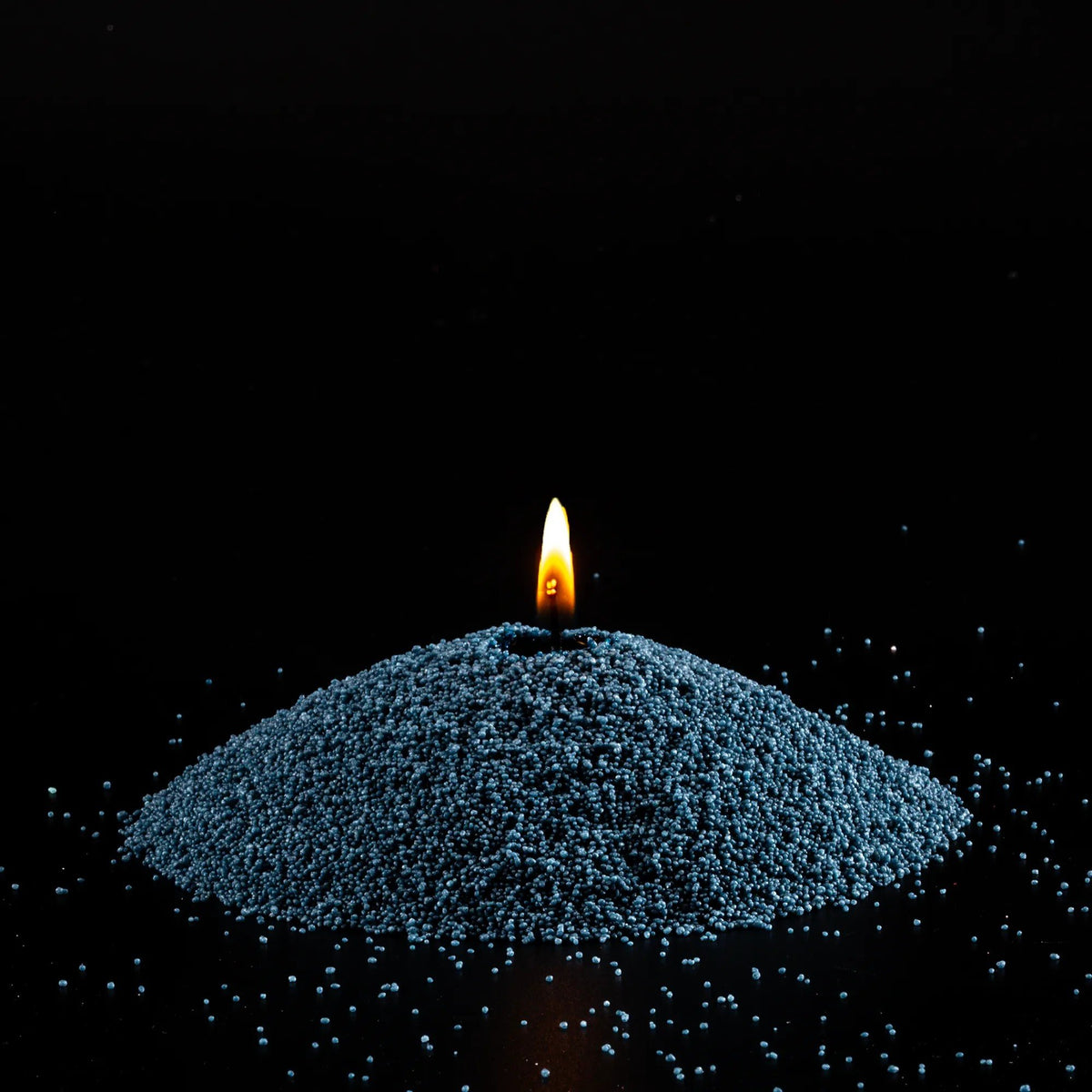 2. Mound of space grey candle sand with lit wick on black background
