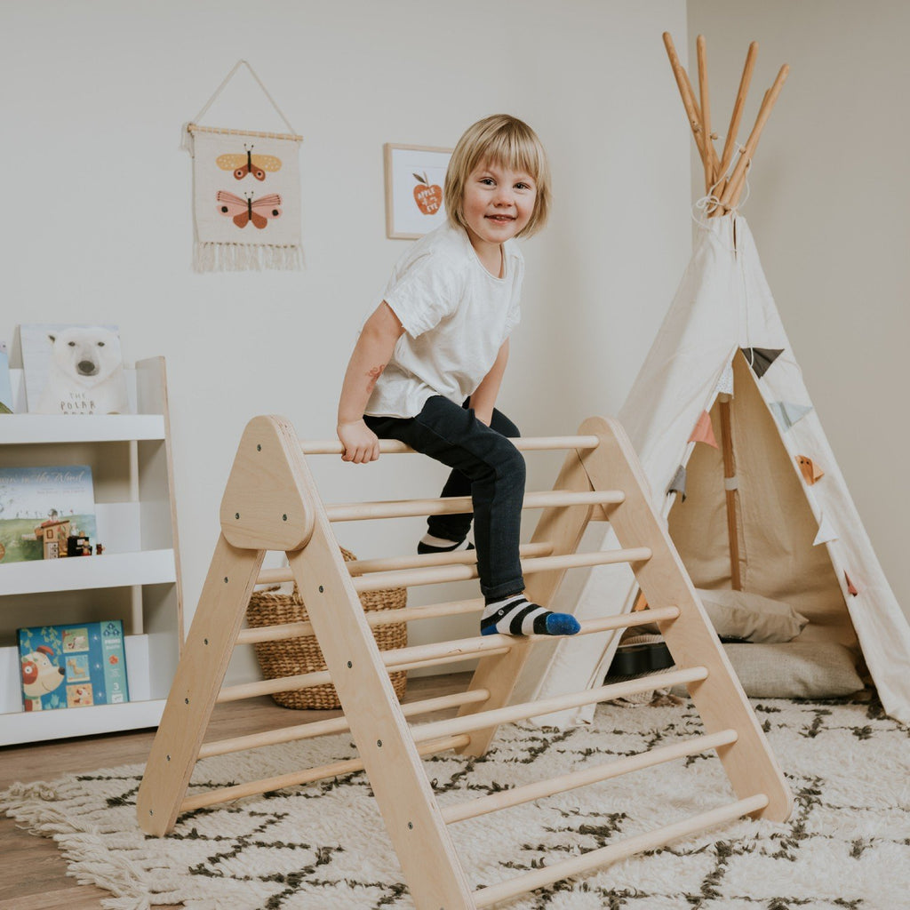 1. Child climbing natural wood Pikler Triangle in playroom with teepee and bookshelves
