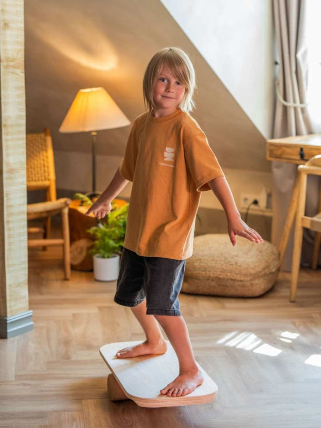 4. Child balancing on rectangular balance board with exercise roll indoors, wearing orange shirt and shorts