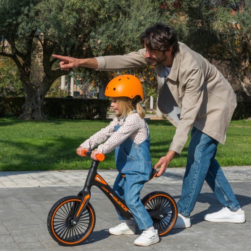 1. Man assisting girl on Feber balance bike in a park setting