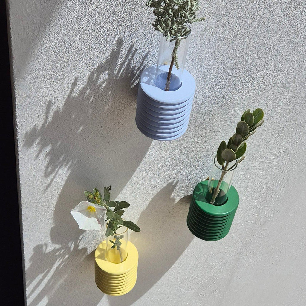 3. Trio of Ribble Wall Vases in green, blue, and yellow by 5mm Paper, displayed on a wall with greenery, lifestyle setting