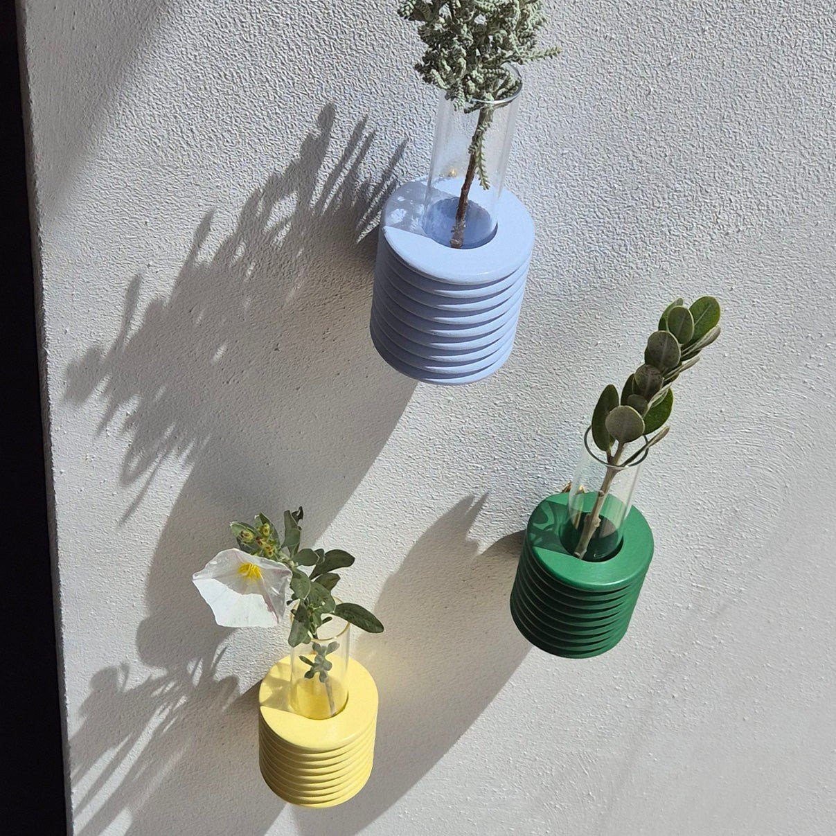 3. Trio of Ribble Wall Vases in green, blue, and yellow by 5mm Paper, displayed on a wall with greenery, lifestyle setting