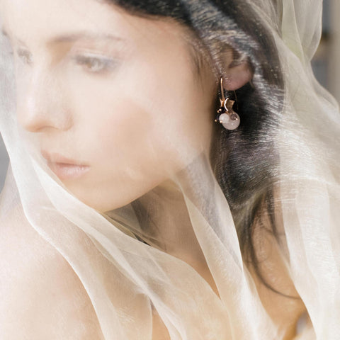1. Woman wearing MyaMoon Richie Black Earrings in rose gold with gemstones, partially veiled, creating a soft, ethereal look