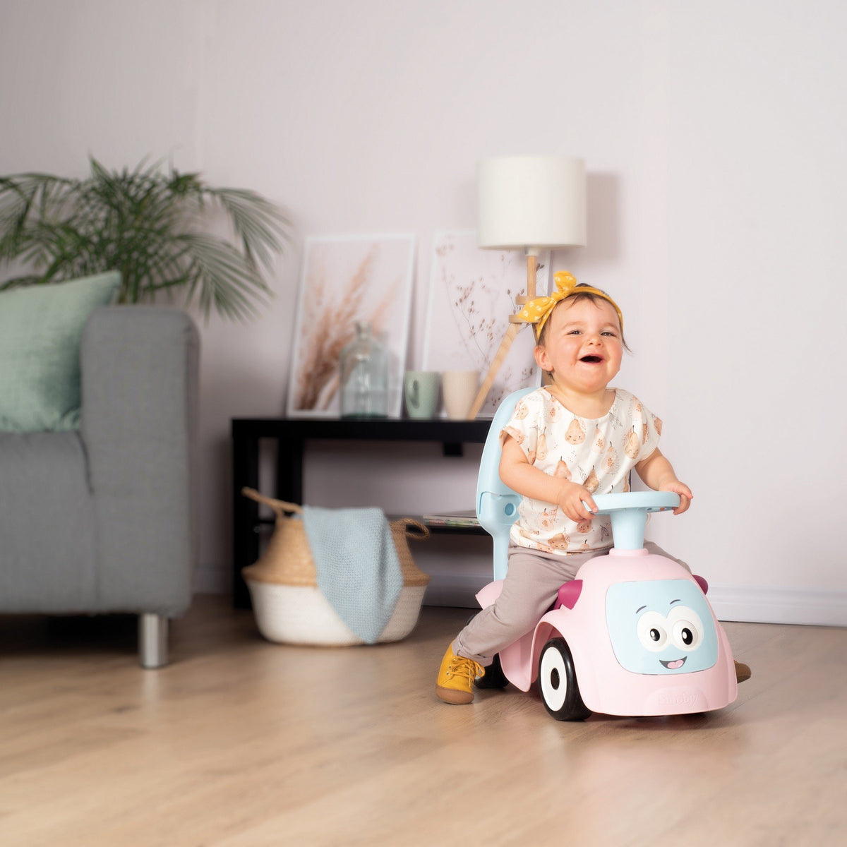4. Child riding Smoby Ride-on Maestro 3in1 in pink indoors, smiling and wearing a yellow headband