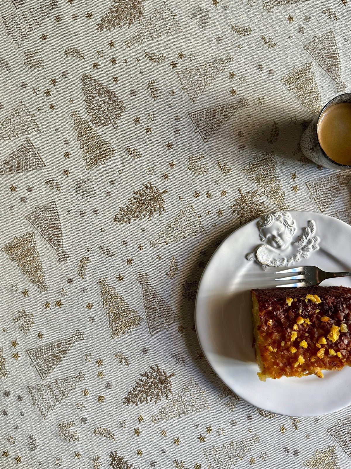 5. Detail of Golden Forest tablecloth with golden tree patterns, set with cake and coffee, enhancing festive dining experience