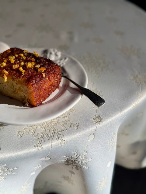 1. Round table with Hortensias Home Golden Snowfall tablecloth, featuring golden snowflake motif, and a dessert plate with cake