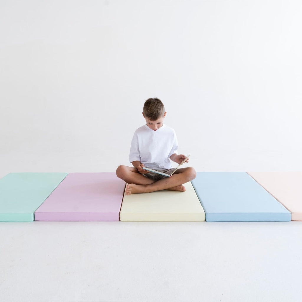 3. Boy sitting cross-legged on pastel mats reading a book, emphasizing comfort and focus in a serene environment