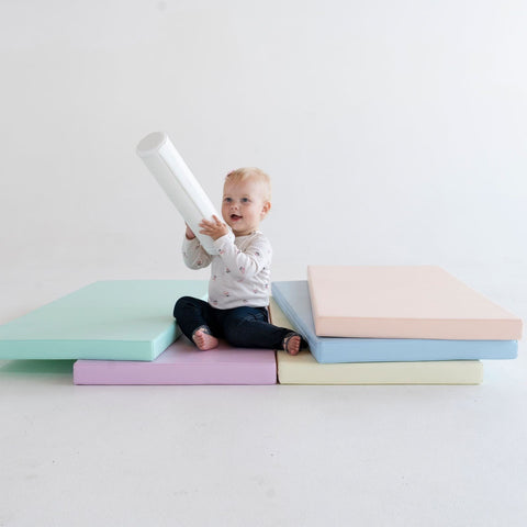 4. Toddler playing with a cylindrical object on pastel mats, illustrating creativity and engagement in a playful setting
