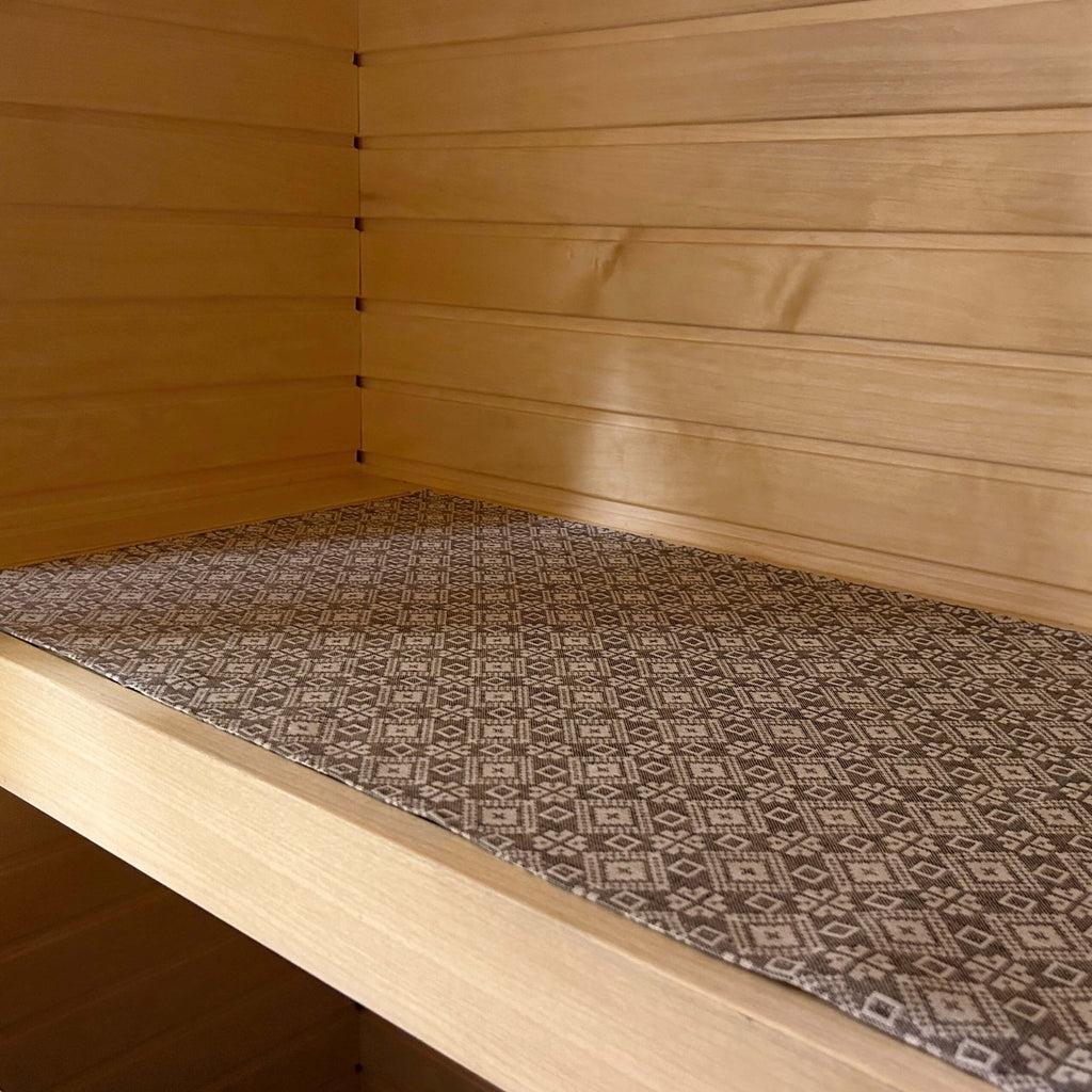 2. Linen and cotton sauna bench seating pad with Tartu County mitten pattern, shown on wooden bench in sauna setting.