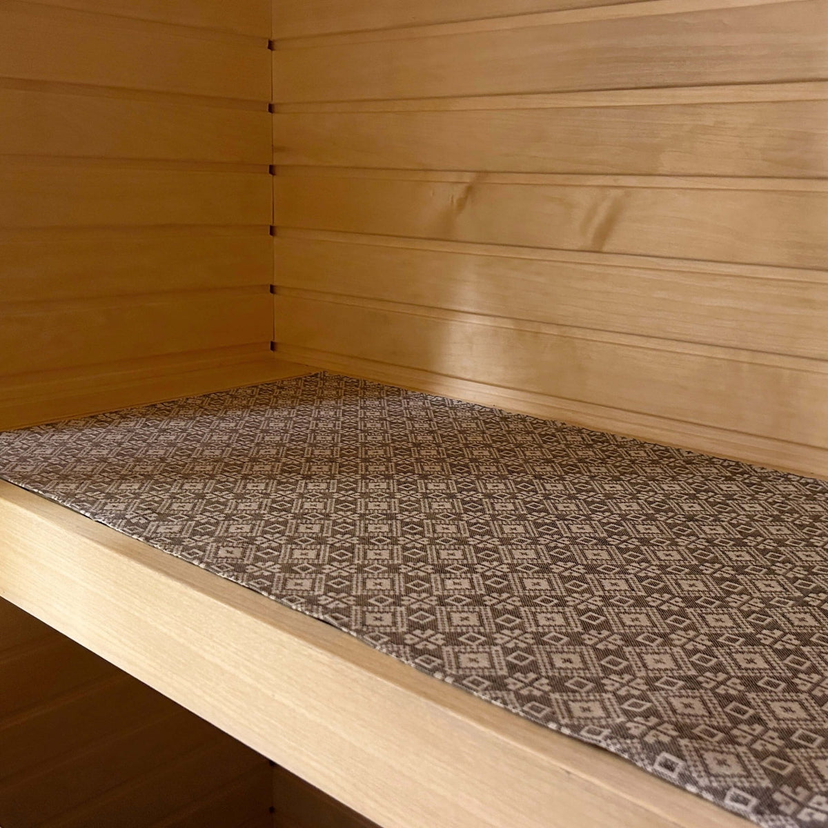 2. Linen and cotton sauna bench seating pad with Tartu County mitten pattern, shown on wooden bench in sauna setting.