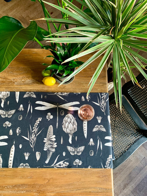 2. Wooden table with Seeds Carbon print table runner, a glass of rosé, and lemons, accented by lush green plants