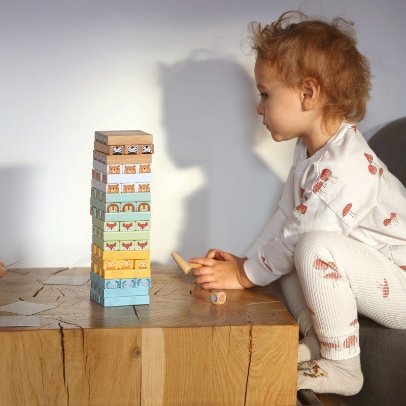 13. Child sitting at a table playing with Shaky Tower game, stacking animal blocks
