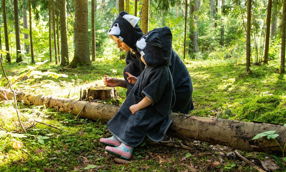 1. Toddlers wearing RÄTT Short-Sleeve Poncho WOLF in a forest setting, showcasing cozy hooded design