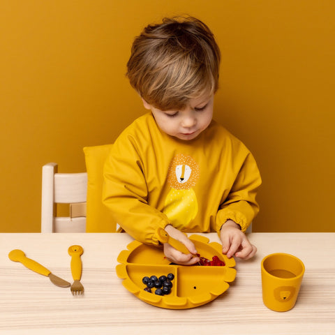3. Child using yellow lion-shaped silicone plate with matching cup and utensils at a wooden table