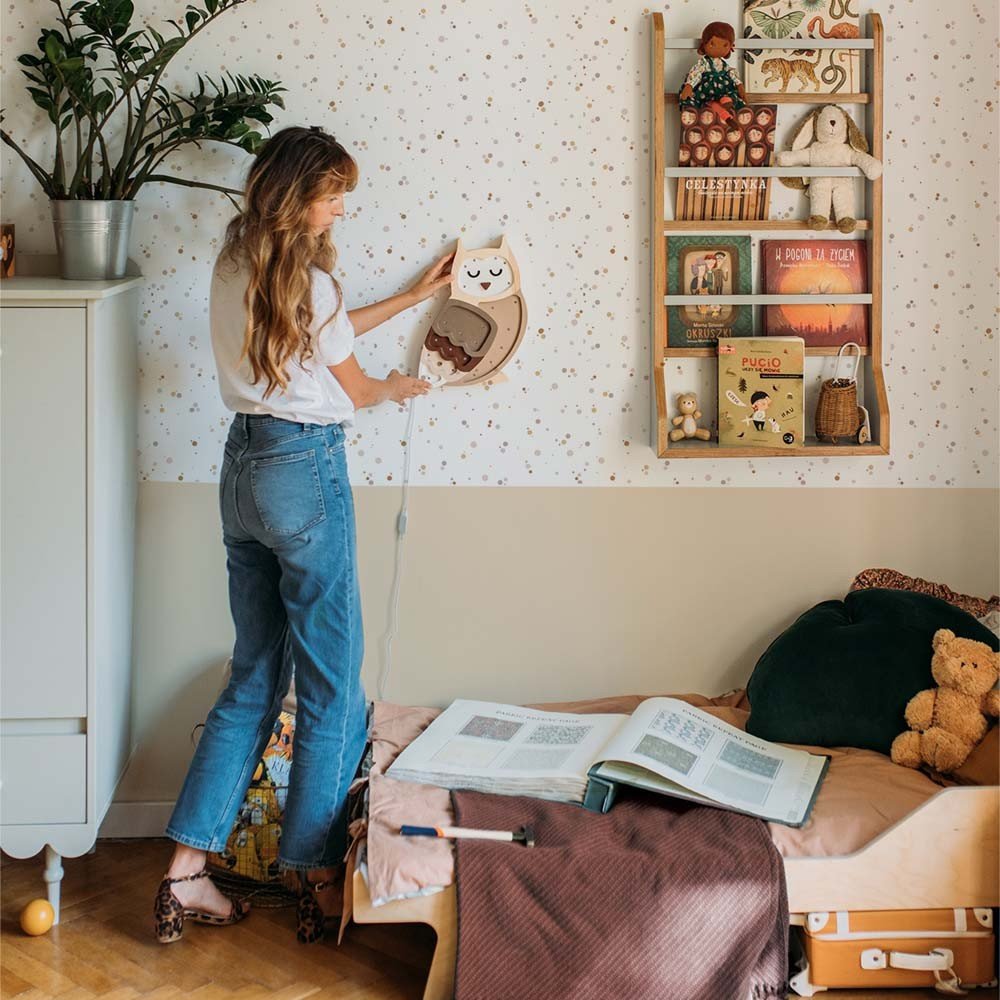 1. Woman decorating child's room with Dekornik Simple Dots Minimini wallpaper and wooden shelf