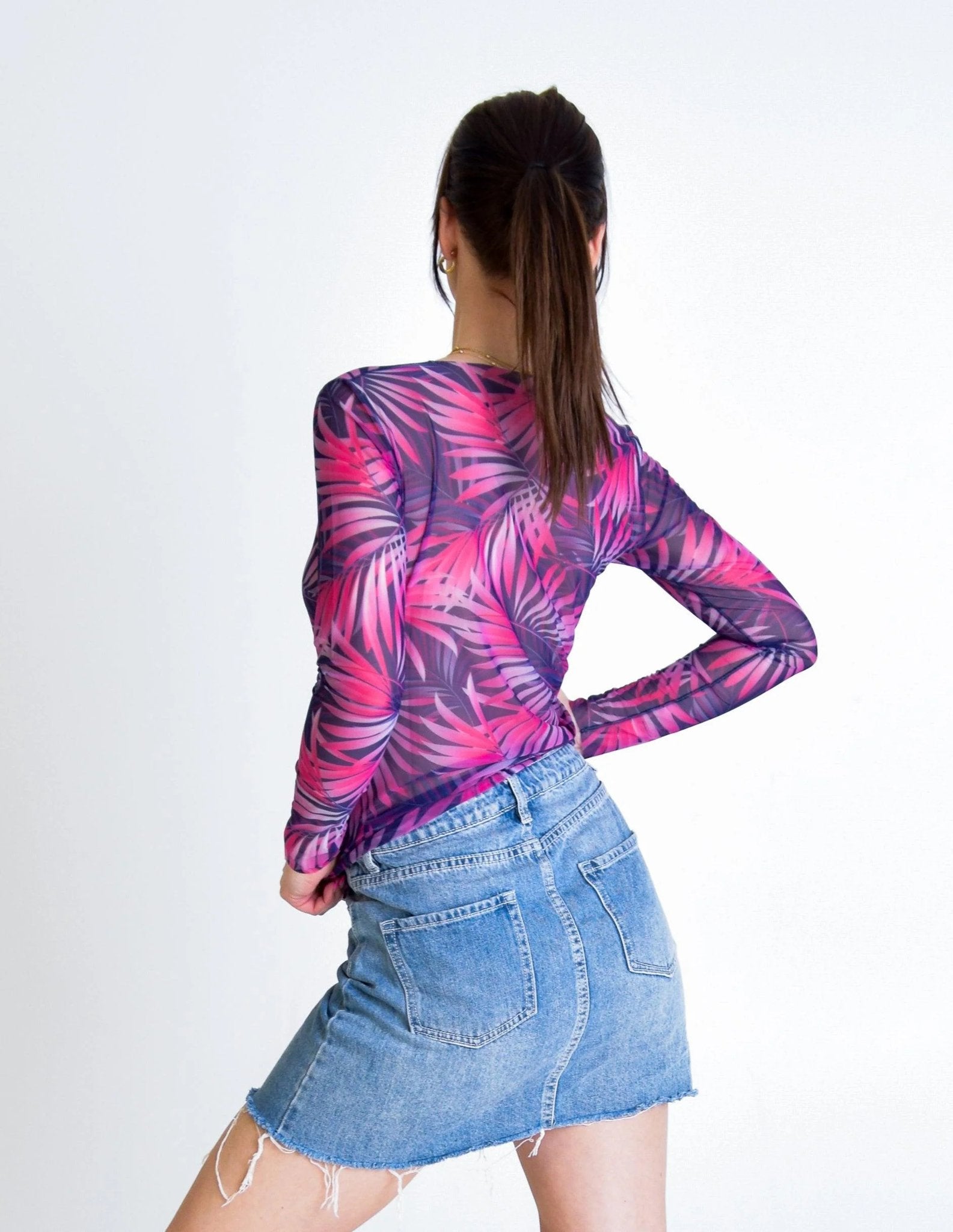 2. Back view of women's pink Tropica tan-through long-sleeve shirt, styled with denim skirt in studio
