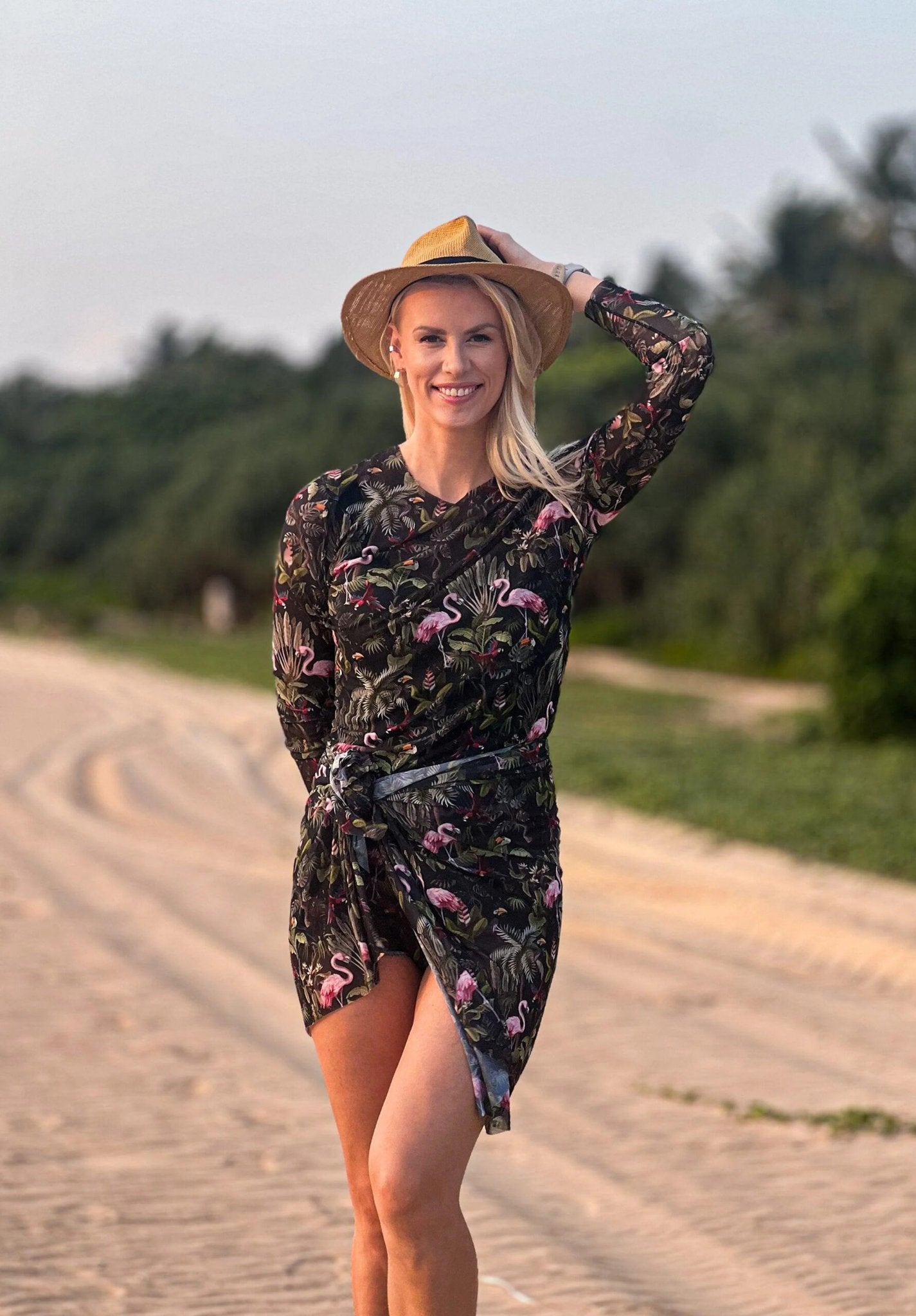 2. Woman wearing Eeva Tropics Tan Through Sarong by Smarttan, styled with a hat on a sandy beach