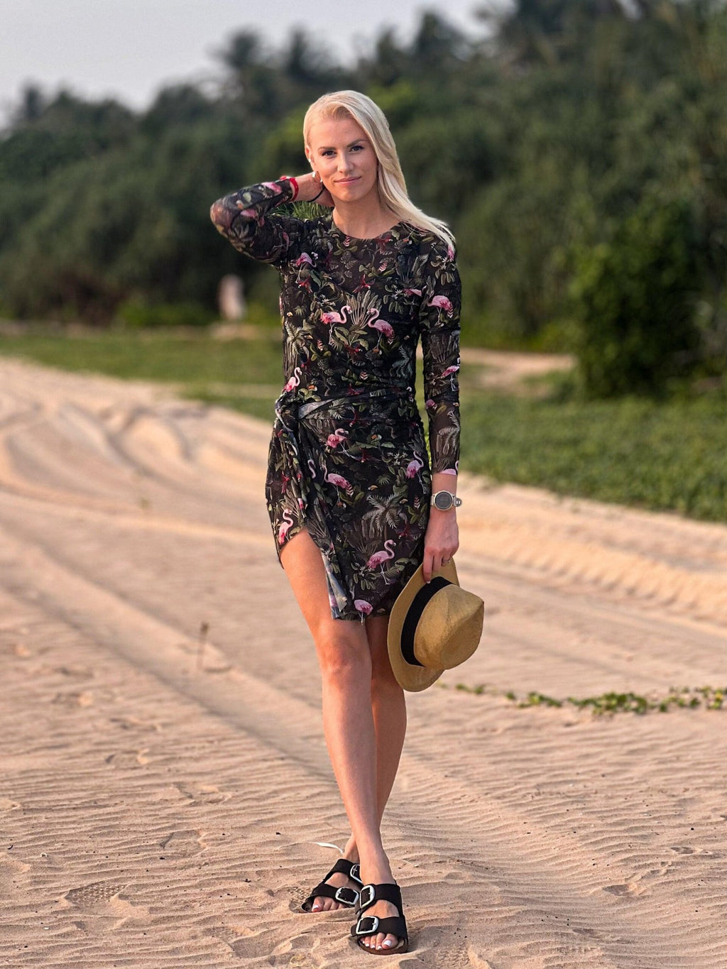 3. Woman in Eeva Tropics Tan Through Sarong by Smarttan, holding a hat, highlighting the vibrant print and beach-ready style