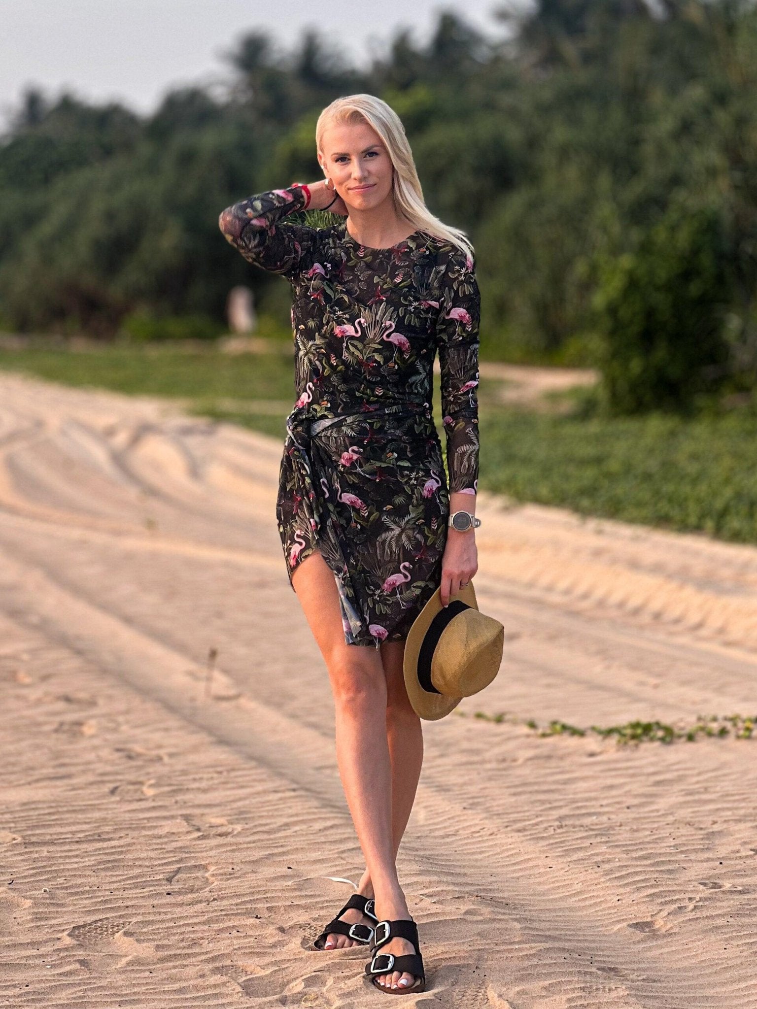 3. Woman in Eeva Tropics Tan Through Sarong by Smarttan, holding a hat, highlighting the vibrant print and beach-ready style