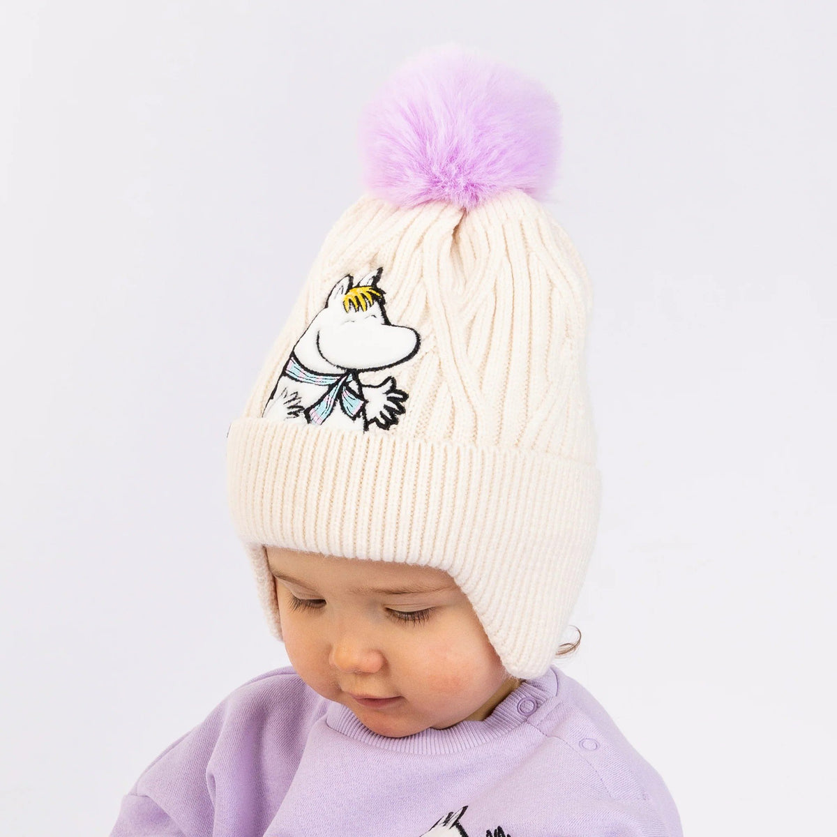 1. Child wearing cream Snorkmaiden winter beanie with purple pom-pom and Moomin character embroidery, in a light setting