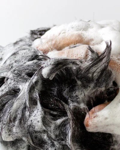 3. Close-up of hands lathering dark hair with shampoo, creating rich foam