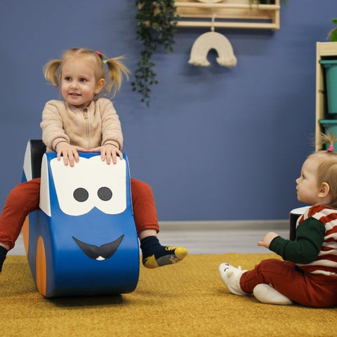 1. Two toddlers playing with IGLU blue soft play ride-on toy car indoors on yellow carpet