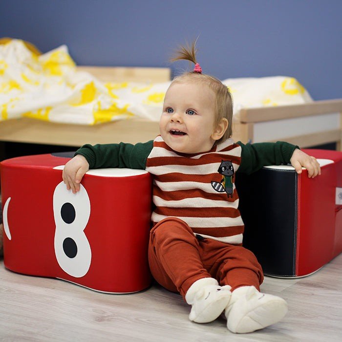 11. Toddler leaning against IGLU red soft play ride-on car toy, smiling indoors