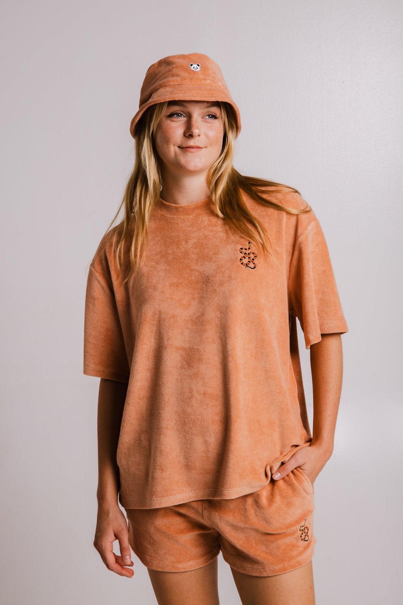 2. Woman in Sossu Coral Snake Terry T-shirt and shorts set in brown, styled with bucket hat, studio setting