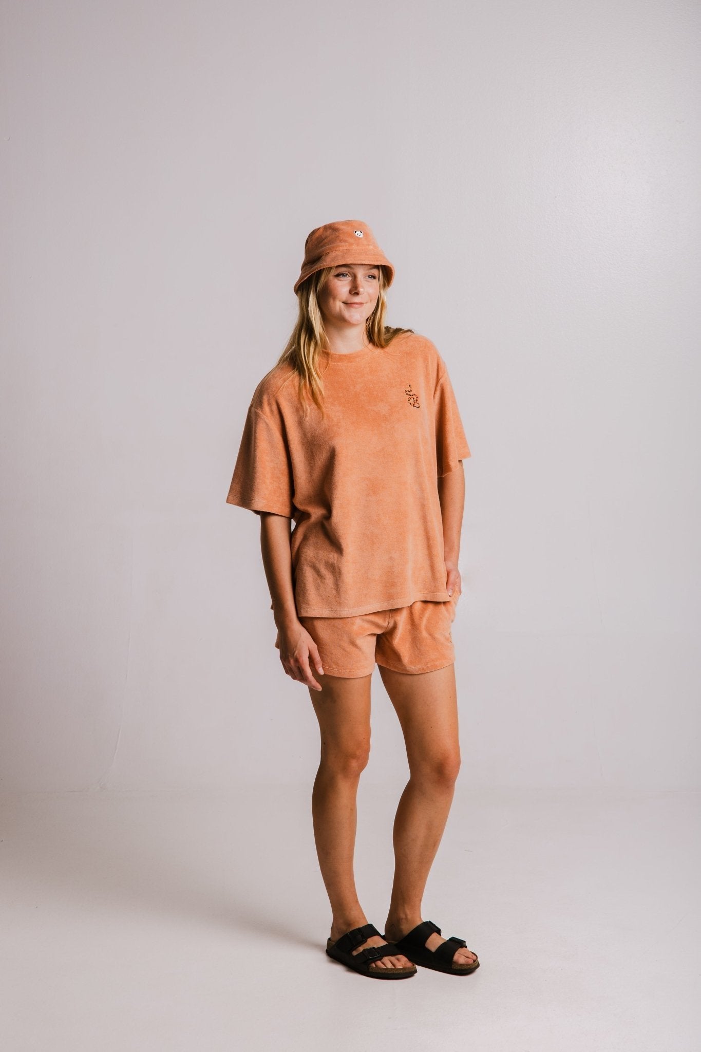 1. Woman wearing Sossu Coral Snake Terry T-shirt in brown with matching shorts and bucket hat, studio setting