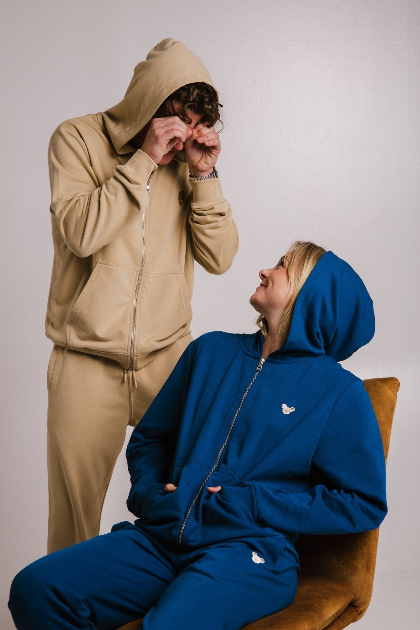5. Unisex Lion Soft Fleece Full Zip Hoodie in light brown worn by male model, blue hoodie worn by female model seated, playful studio setting