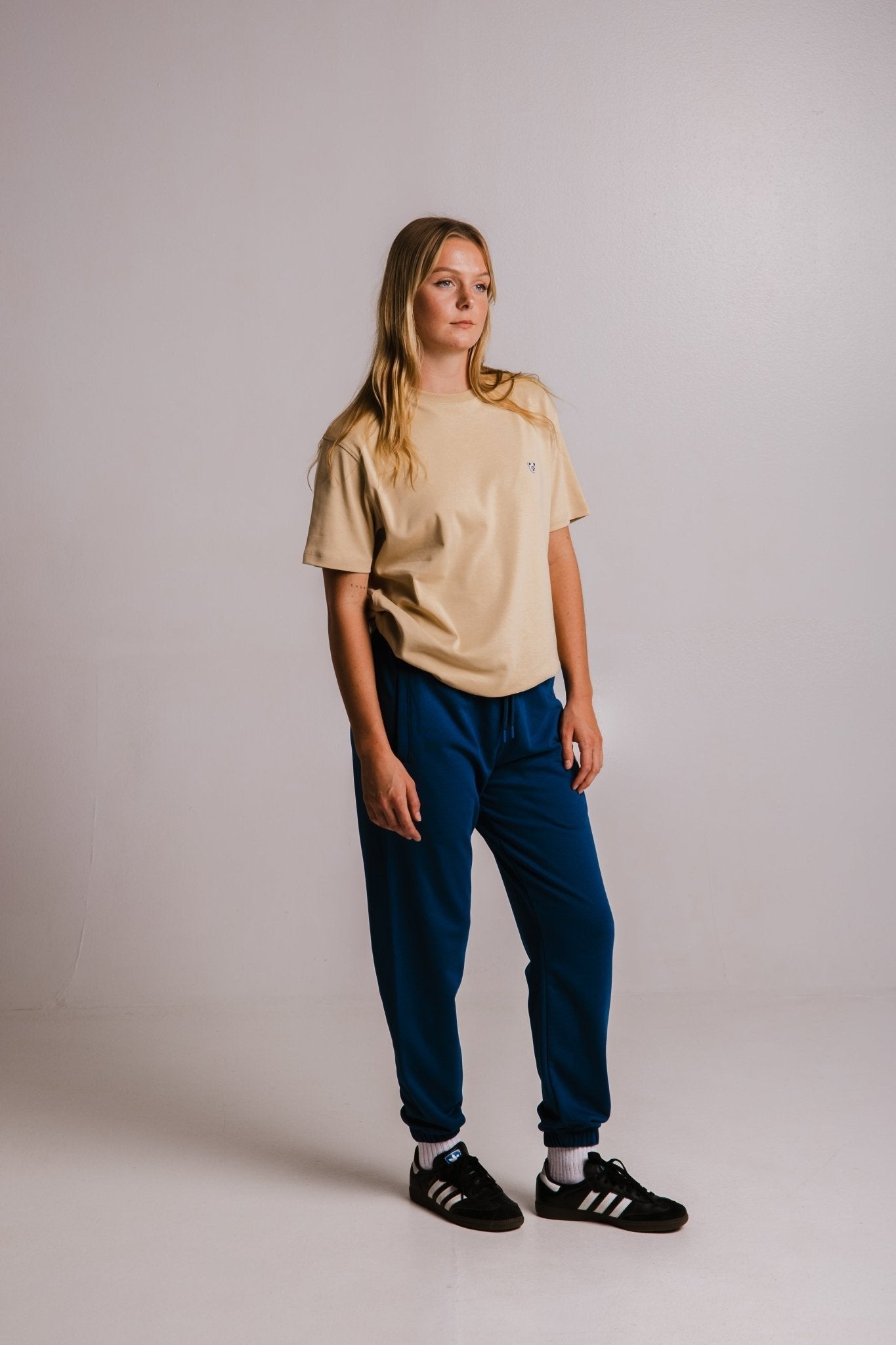 2. Women's Panda Heavy T-shirt in light brown by Sossu, paired with blue pants in a studio setting