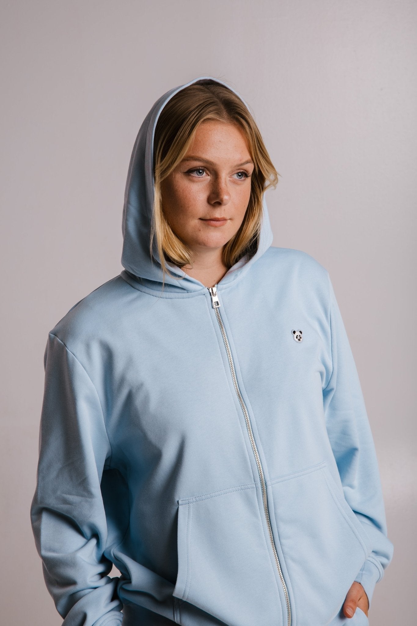6. Woman in Sossu light blue Panda Soft Fleece Full Zip Hoodie with hood up, studio shot