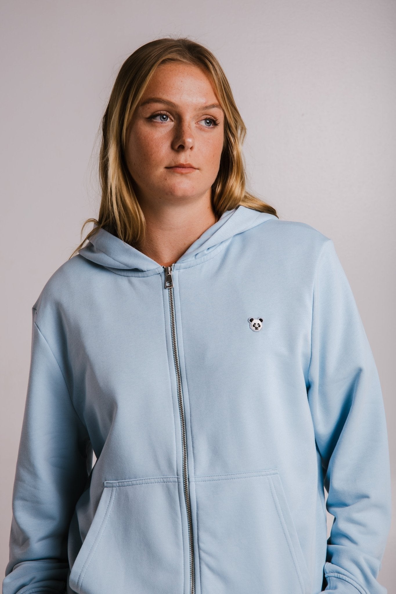 3. Front view of woman wearing Sossu light blue Panda Soft Fleece Full Zip Hoodie, studio setting