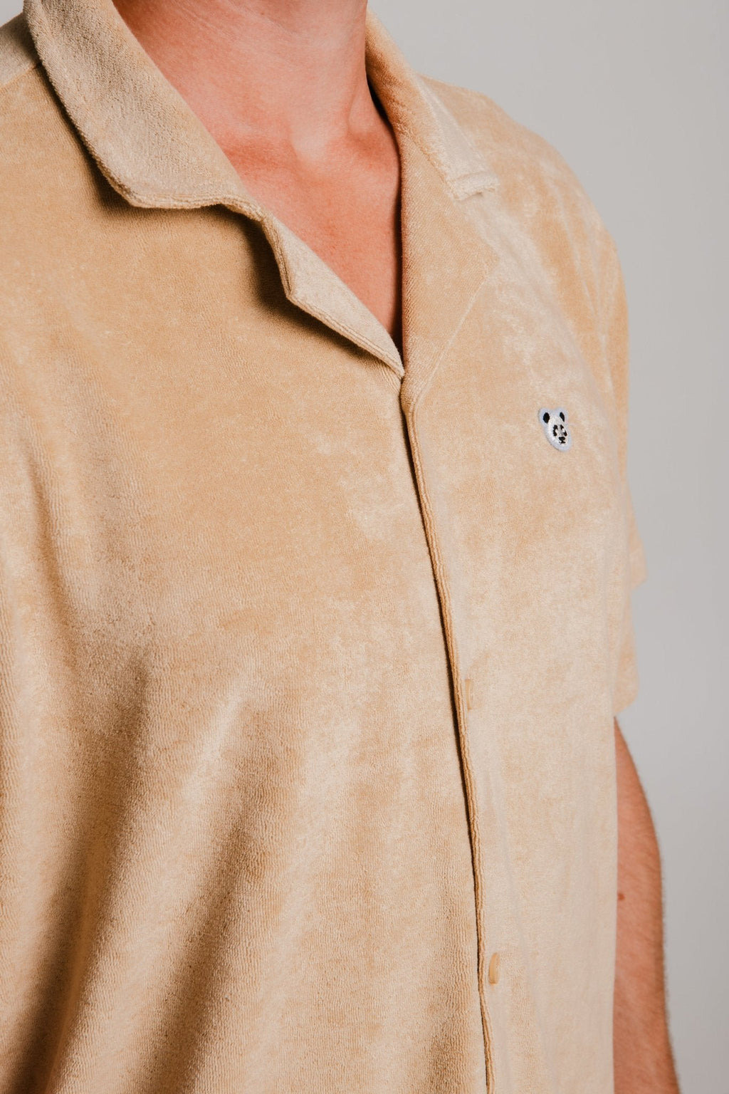 5. Close-up of Sossu Panda Terry Shirt in light brown highlighting fabric texture and panda embroidery, studio setting