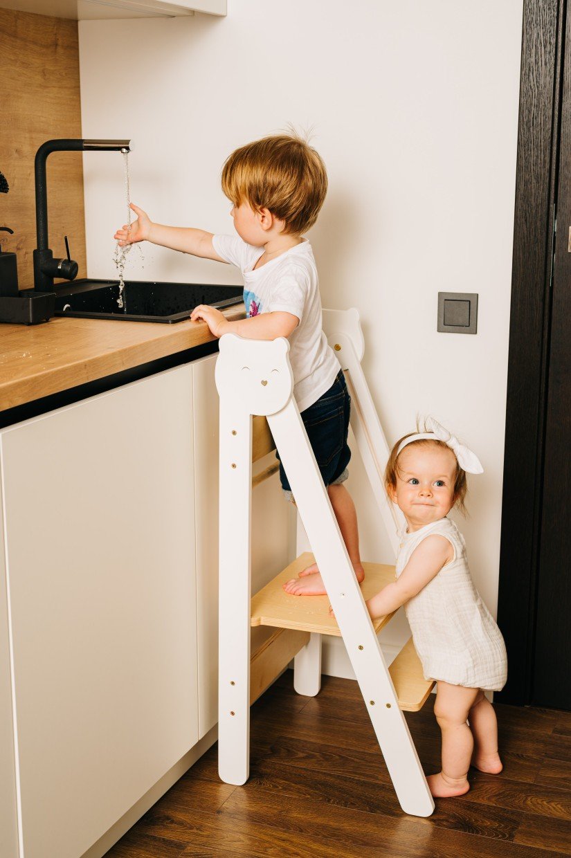 16. Two children using white step stool in kitchen