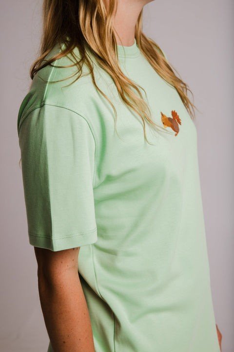4. Side view of Sossu Squirrel Heavy T-shirt in light green, showing fit and embroidered design, worn by woman