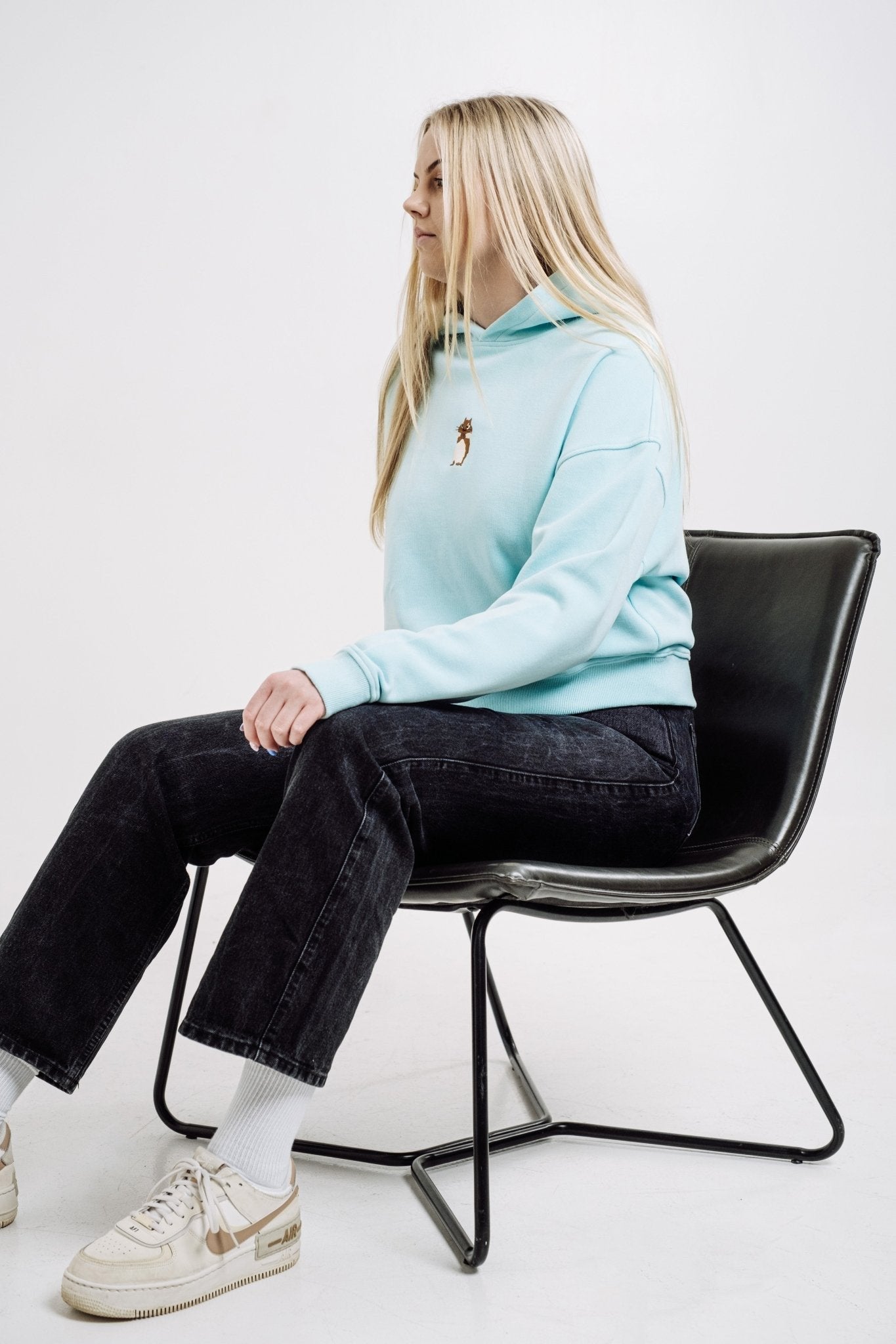 3. Woman seated wearing Sossu Squirrel Hoodie in mint, emphasizing casual style and embroidered detail