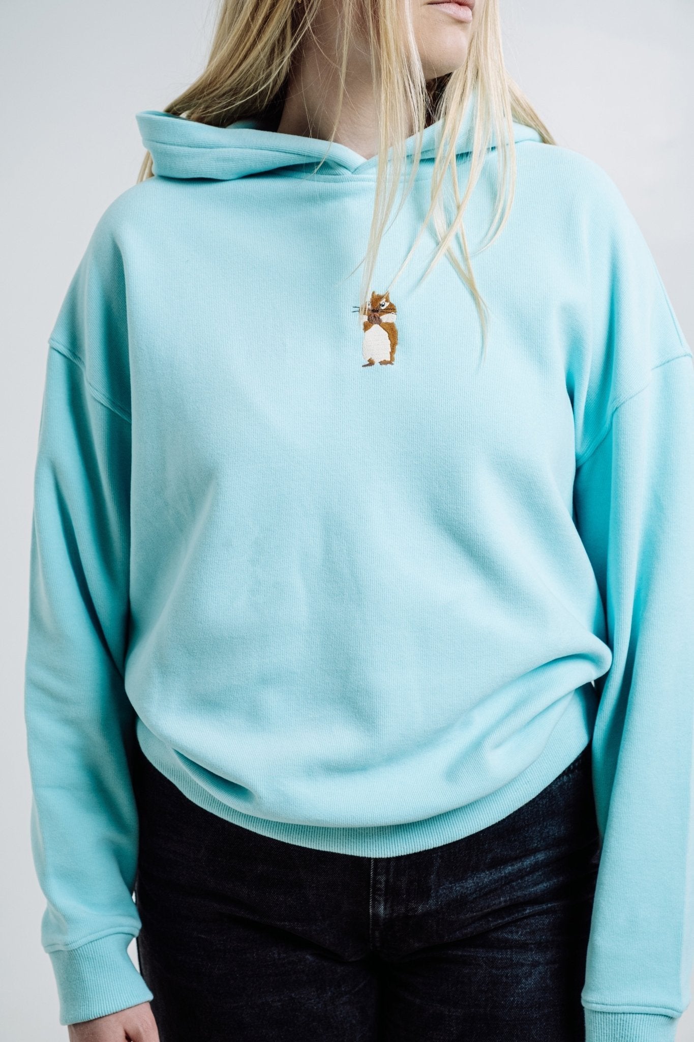 4. Close-up of woman in Sossu Squirrel Hoodie in mint, showing embroidered squirrel detail