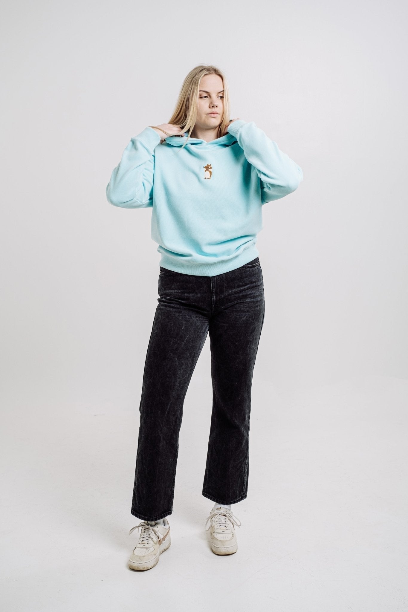1. Woman wearing Sossu Squirrel Hoodie in mint, showcasing relaxed fit and embroidered detail in studio setting