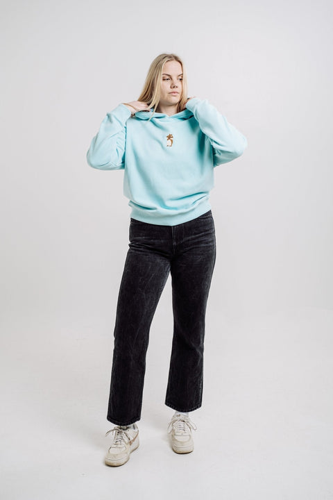 1. Woman wearing Sossu Squirrel Hoodie in mint, showcasing relaxed fit and embroidered detail in studio setting