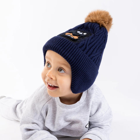1. Child wearing navy blue Moomin Stinky beanie with brown pom-pom, smiling on white background