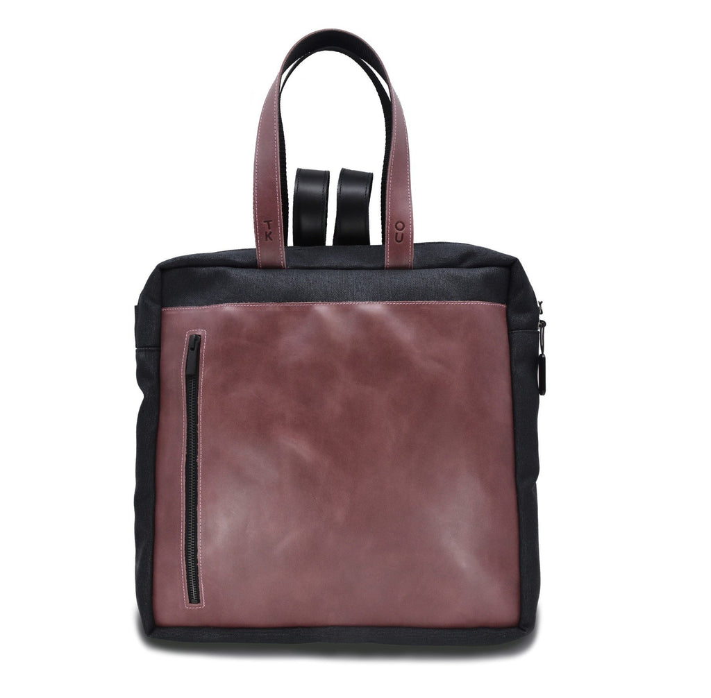 2. Studio image of the Omaking Stockholm Backpack in purple and black, highlighting the front zippered pocket and dual handles