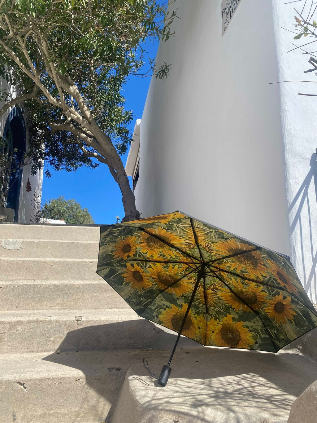 1. Sunflower umbrella with bright sunflower design resting on outdoor stone steps under clear blue sky