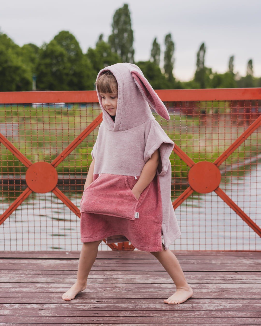 1. Child in pink Surfbunny bath poncho with bunny ears standing on wooden deck
