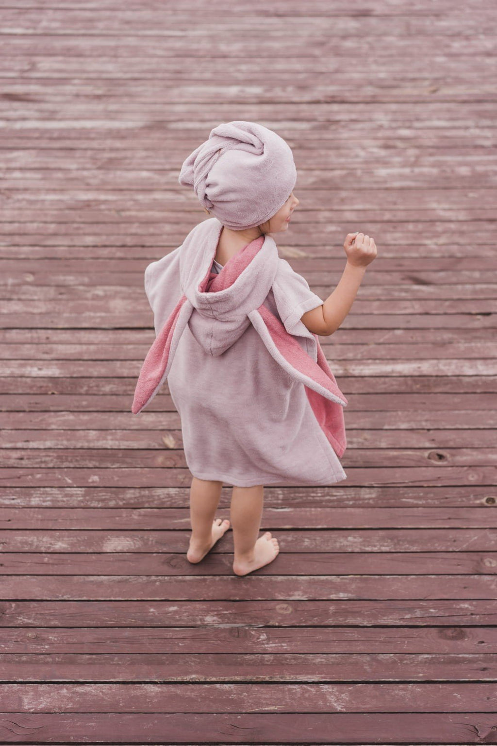 1. Child in pink Surfbunny bath poncho with bunny ears shown from back on wooden deck