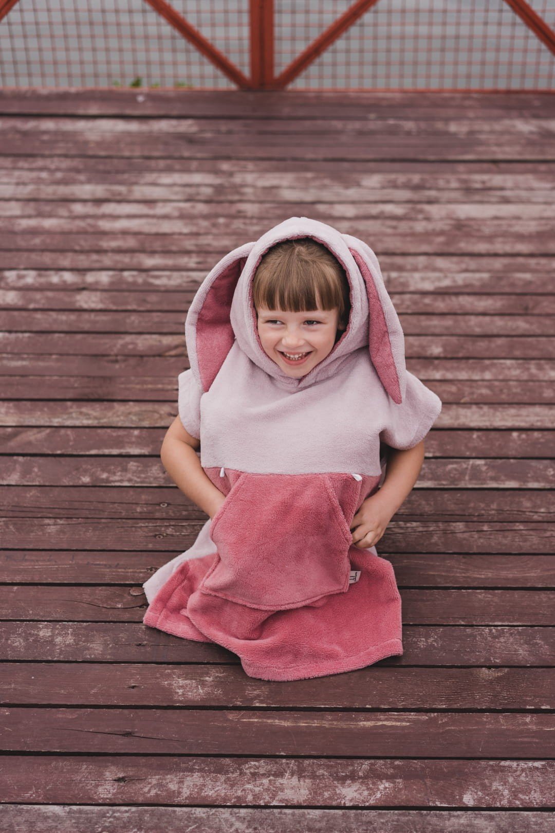 1. Child wearing pink Surfbunny bath poncho with bunny ears on a wooden deck