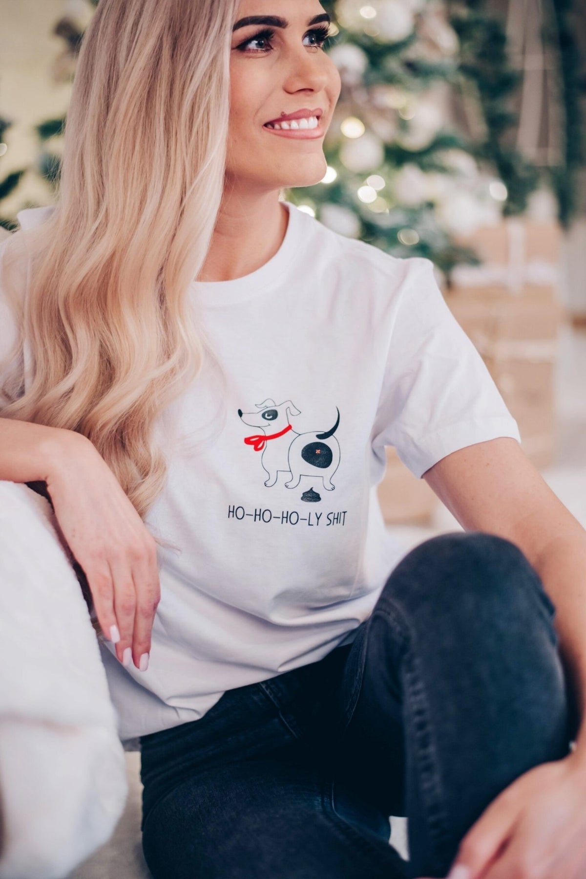 1. Woman sitting indoors wearing white T-shirt with dog graphic and 'Ho-ho-ho-ly sh*t' text, smiling