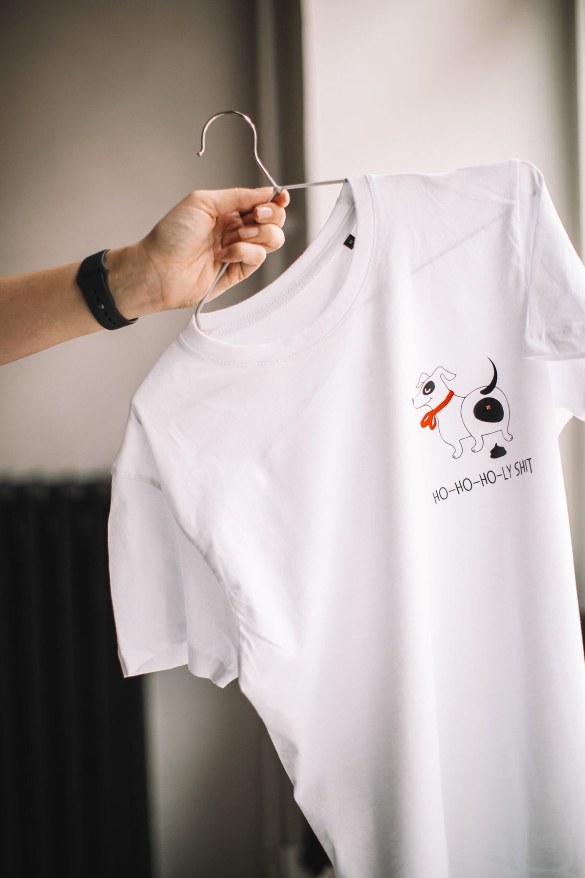 2. White T-shirt with dog graphic and 'Ho-ho-ho-ly sh*t' text held on hanger, showcasing design